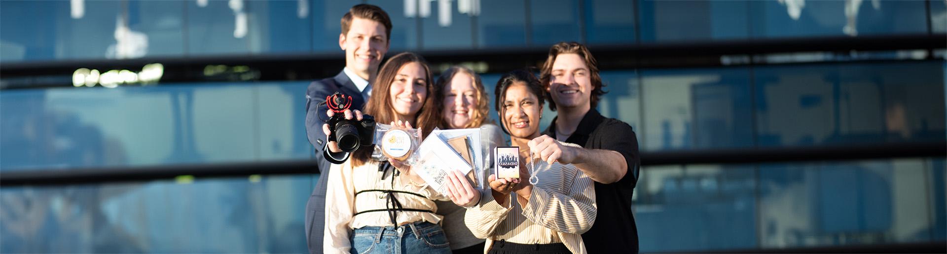 Five students smiling and holding up products from their entrepreneurial businesses.